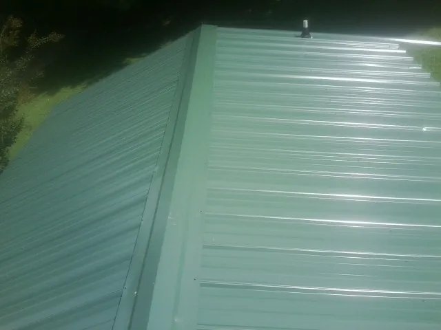 New green metal panels meeting at the ridge of a roof — Flat Roof Repair work by our crew in Gloucester City