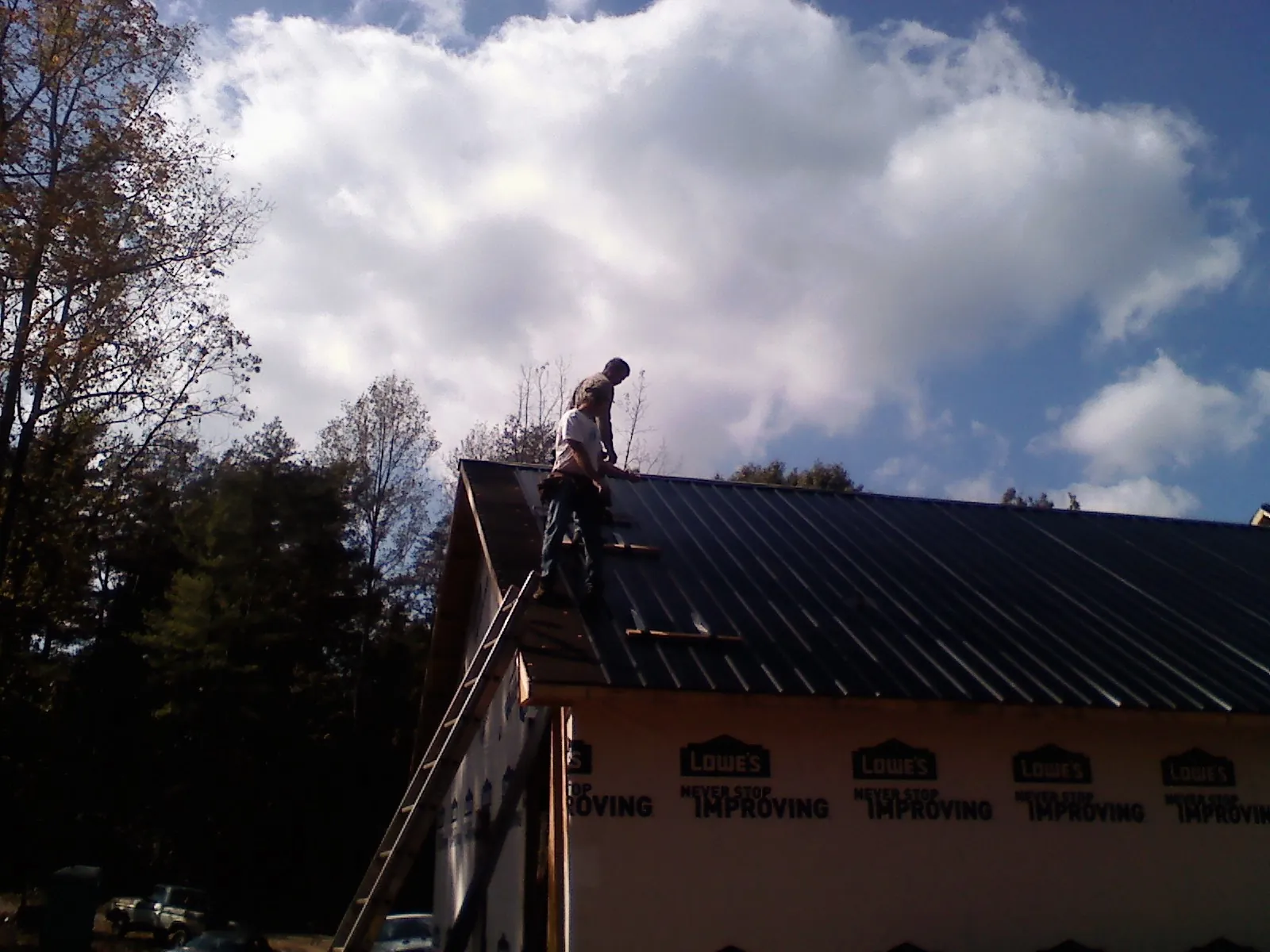 Roofer fastening dark metal panels high against a cloudy sky, from a Roof Inspection job in Gloucester City