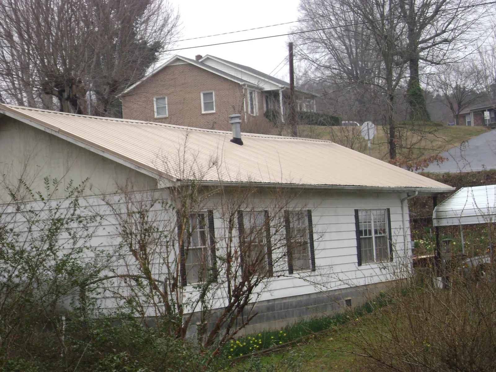 Tan metal roof on a white sided house set into a hillside — Commercial Roofing by Roofing Brothers in Gloucester City